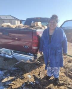 Native American woman smiles next to truck full of firewood