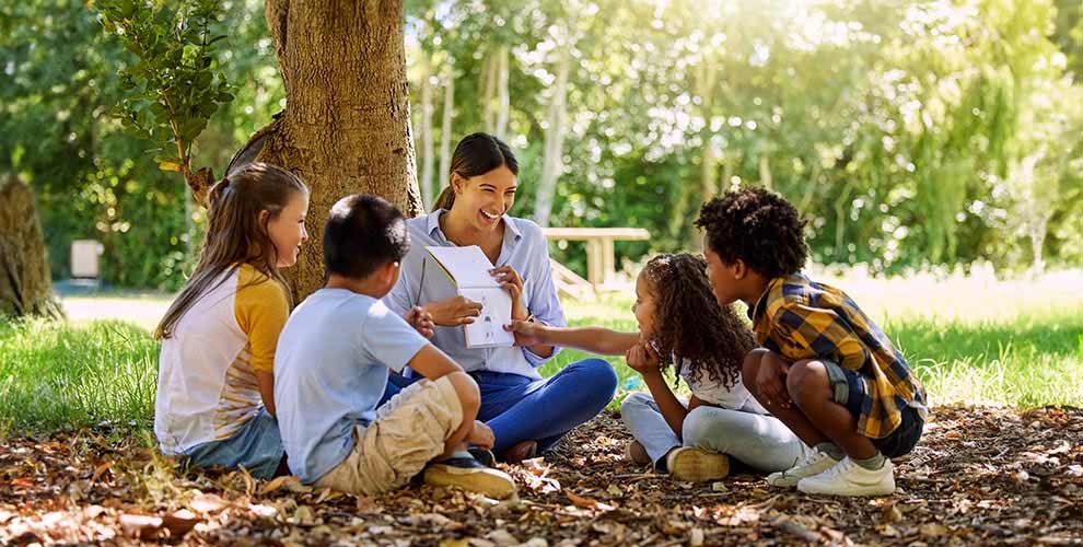 Camp counselor and four kids sitting outside under a tree