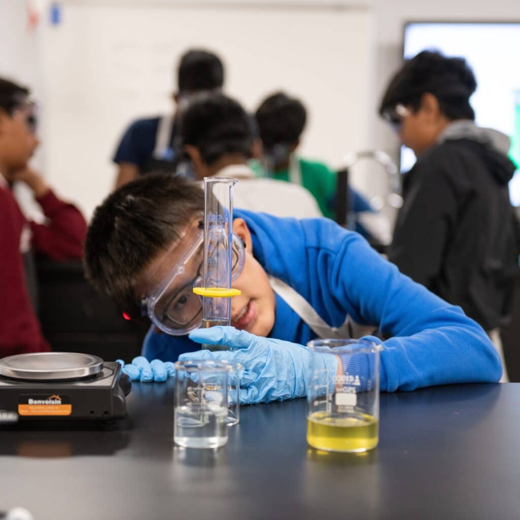 Student wearing gloves and goggles looks into beaker