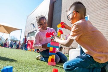 Two kindergarten children playing outside, building a tower of a blocks